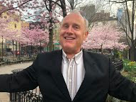 James smiles at the camera, wearing a suit and standing in front of cherry blossoms.