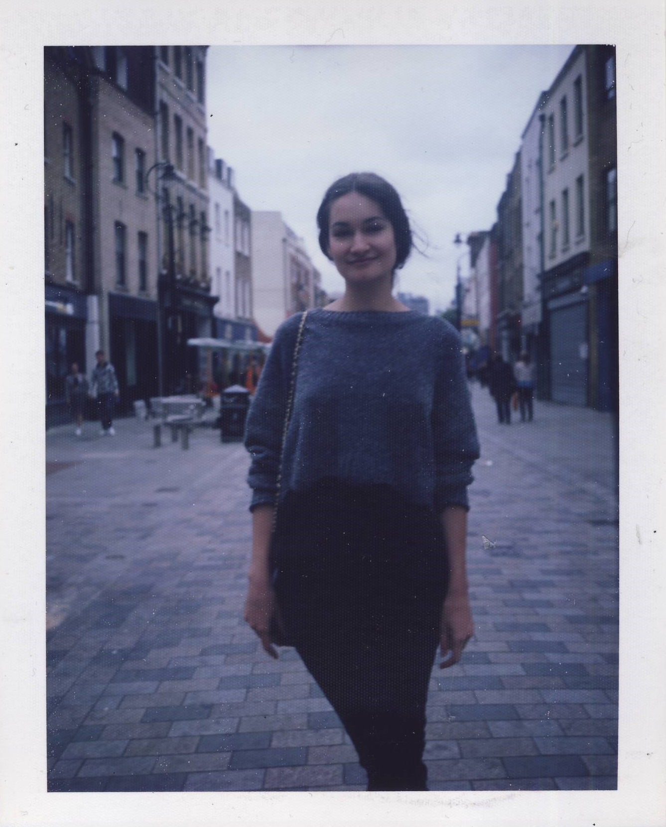 A polaroid of Eva standing in the street and smiling at the camera.
