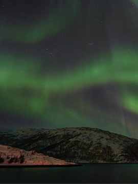 The northern lights in shades of emerald green over snowy mountains.