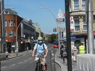 A cyclist in a blue shirt with a matching face mask riding on a street in what looks like London.