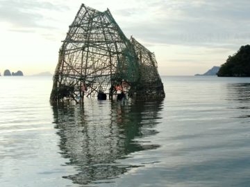 A sculpture in the sea with islands behind it.